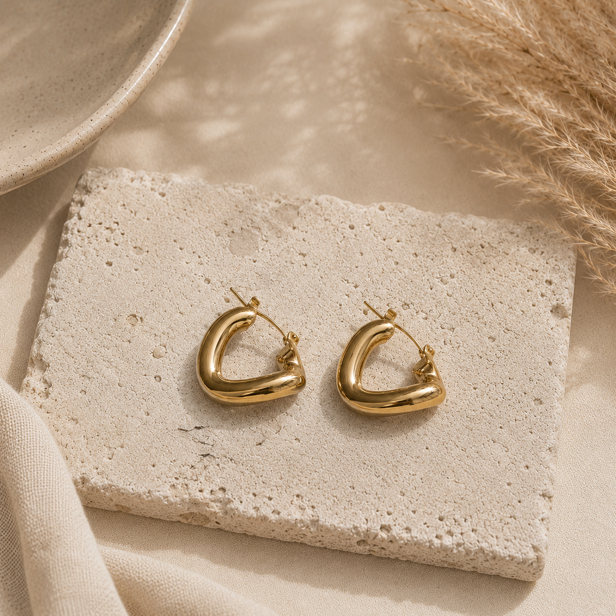 Chunky goudkleurige hoops Atlas Earrings van hi SISU op travertin steen