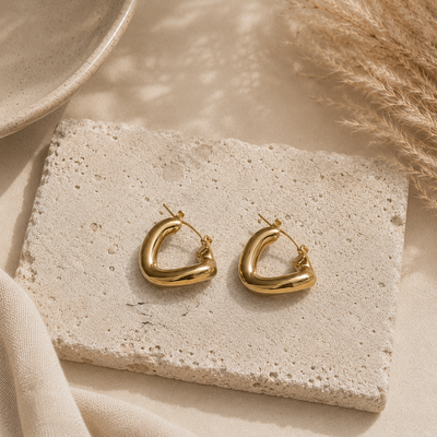 Chunky goudkleurige hoops Atlas Earrings van hi SISU op travertin steen