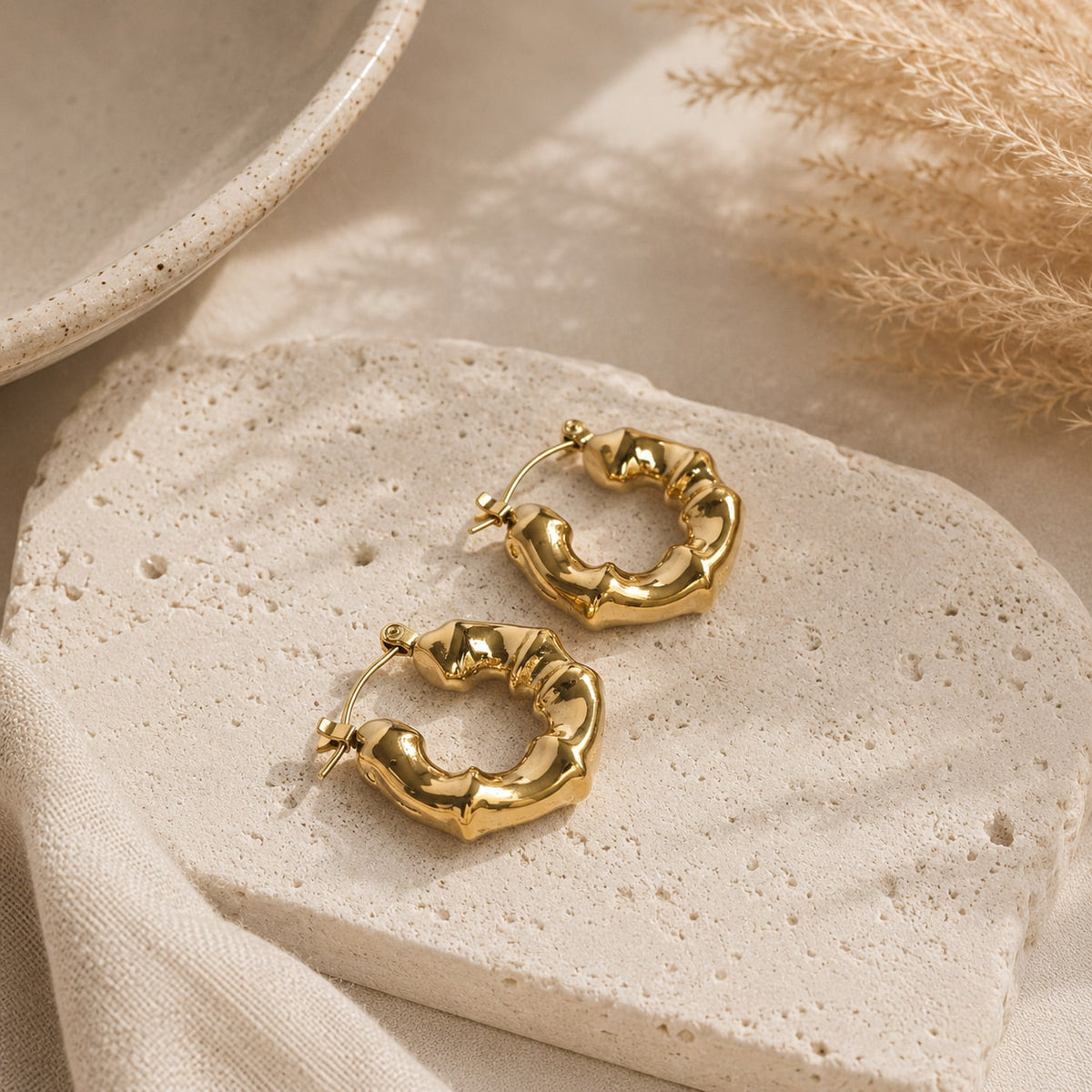 Golvende gouden oorringen met bamboe-design op zonnige steen