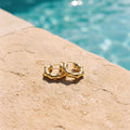 Kleine goudkleurige hoops Aubrey Earrings van hi SISU aan de rand van een zwembad