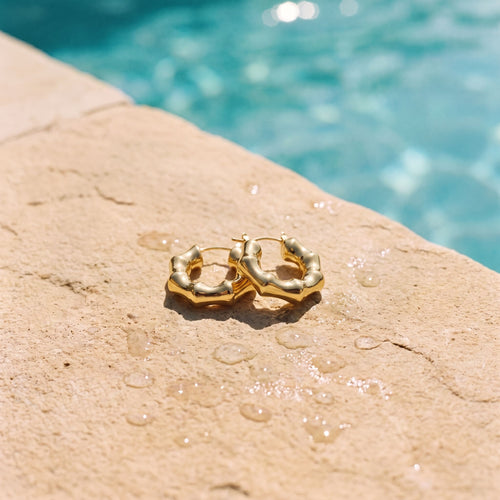 Kleine goudkleurige hoops Aubrey Earrings van hi SISU aan de rand van een zwembad