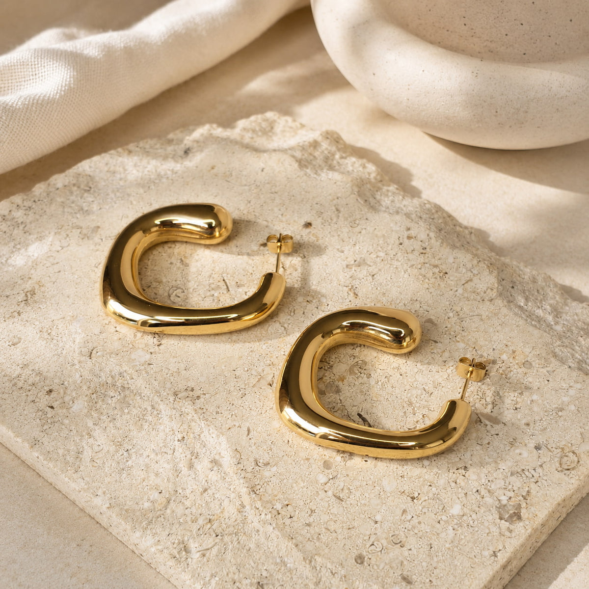 Gouden chunky hoops Blair Earrings met zachte hoekige vorm, op travertin steen bij hi SISU