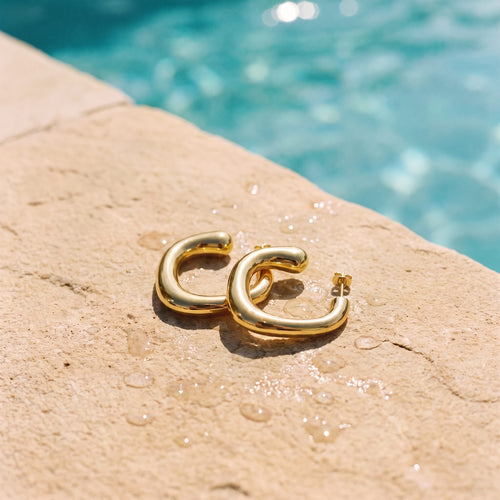 Chunky goudkleurige hoops Blair Earrings van hi SISU aan de rand van een zwembad
