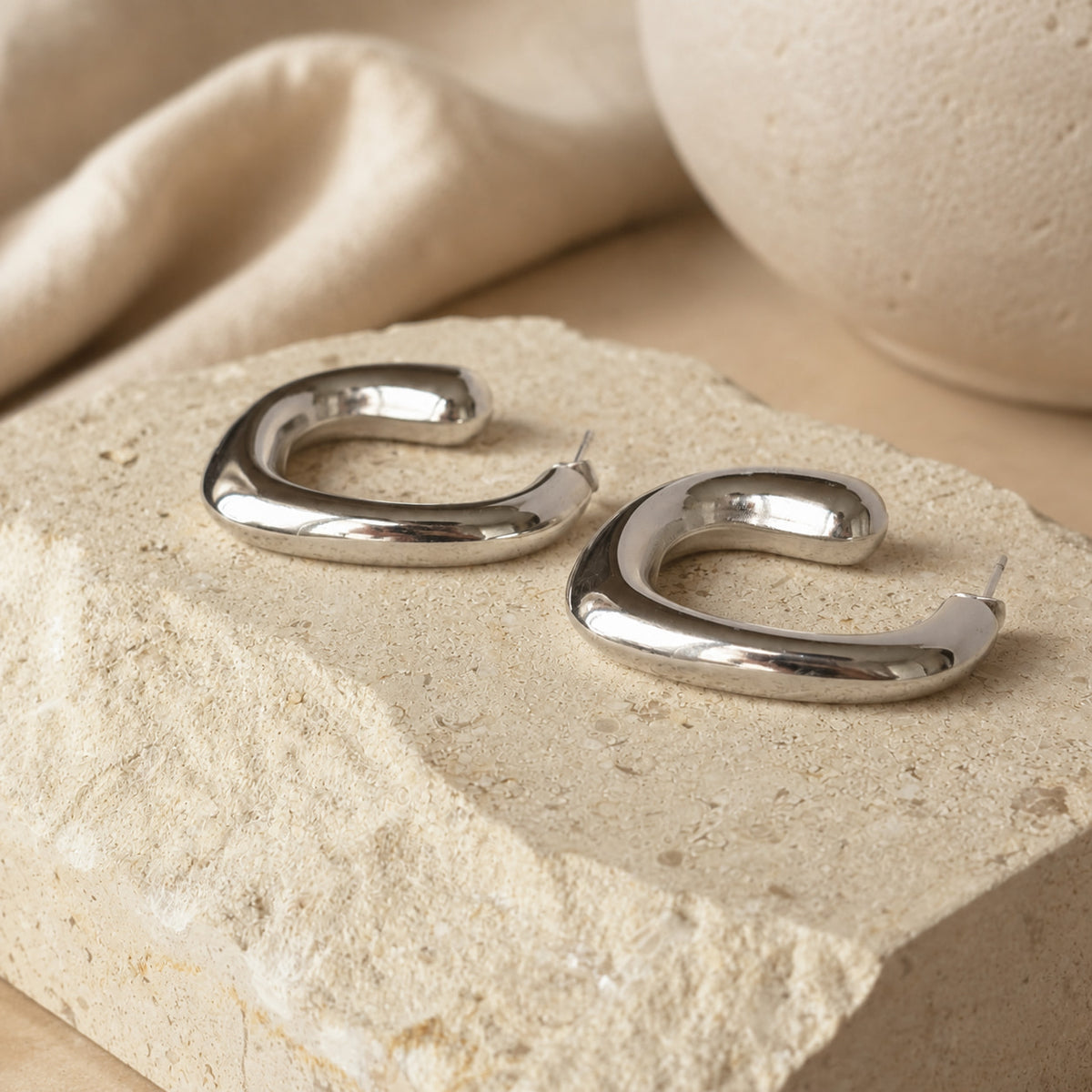 Zilverkleurige chunky hoops Blair Earrings van hi SISU op travertin steen