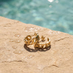 Kleine gouden oorringen met Cuban link design aan de rand van een zwembad