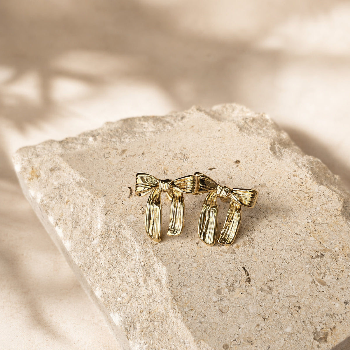 Gouden strik oorbellen Sage Earrings van hi SISU met ribbeltextuur, op travertin steen