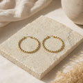 Grote goudkleurige twisted hoops Chloe Earrings van hi SISU op travertin steen
