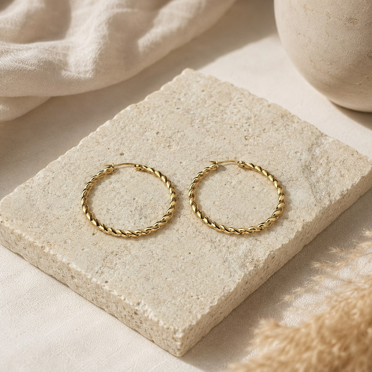 Grote goudkleurige twisted hoops Chloe Earrings van hi SISU op travertin steen