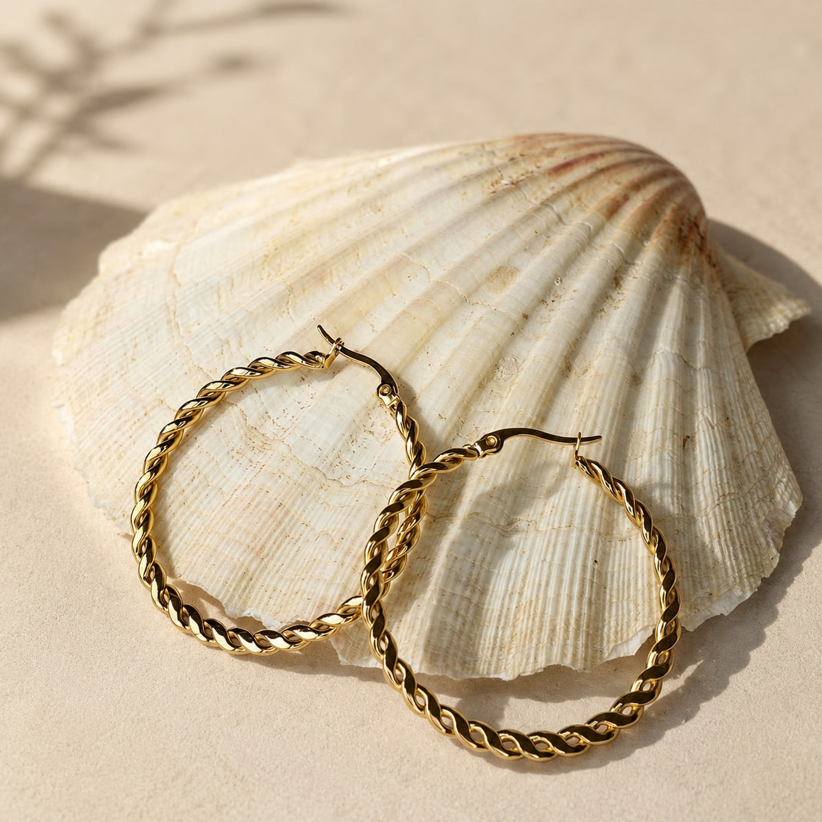 Grote gouden twisted hoops Chloe Earrings van hi SISU tegen een schelp op het strand