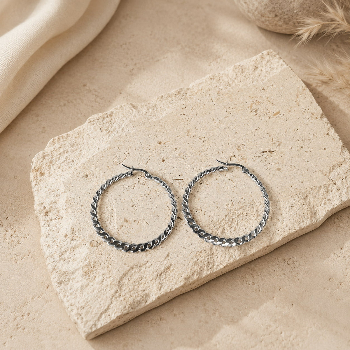 Zilverkleurige twisted hoops Chloe Earrings van hi SISU, flatlay op travertin steen