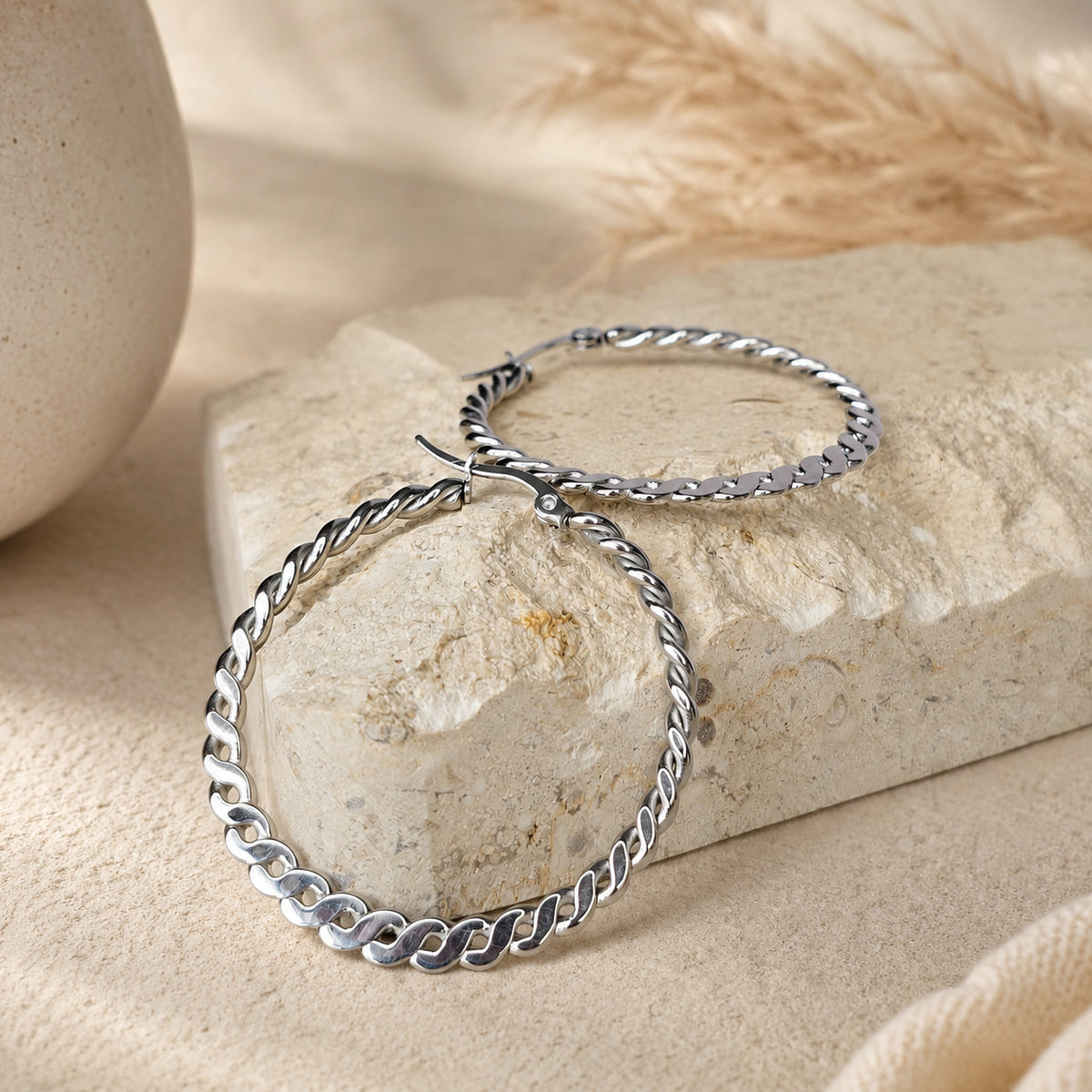 Grote zilveren oorringen met gedraaid design, Chloe Earrings van hi SISU tegen travertin steen