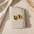 Goudkleurige teardrop oorbellen Isabel Earrings van hi SISU op travertin steen