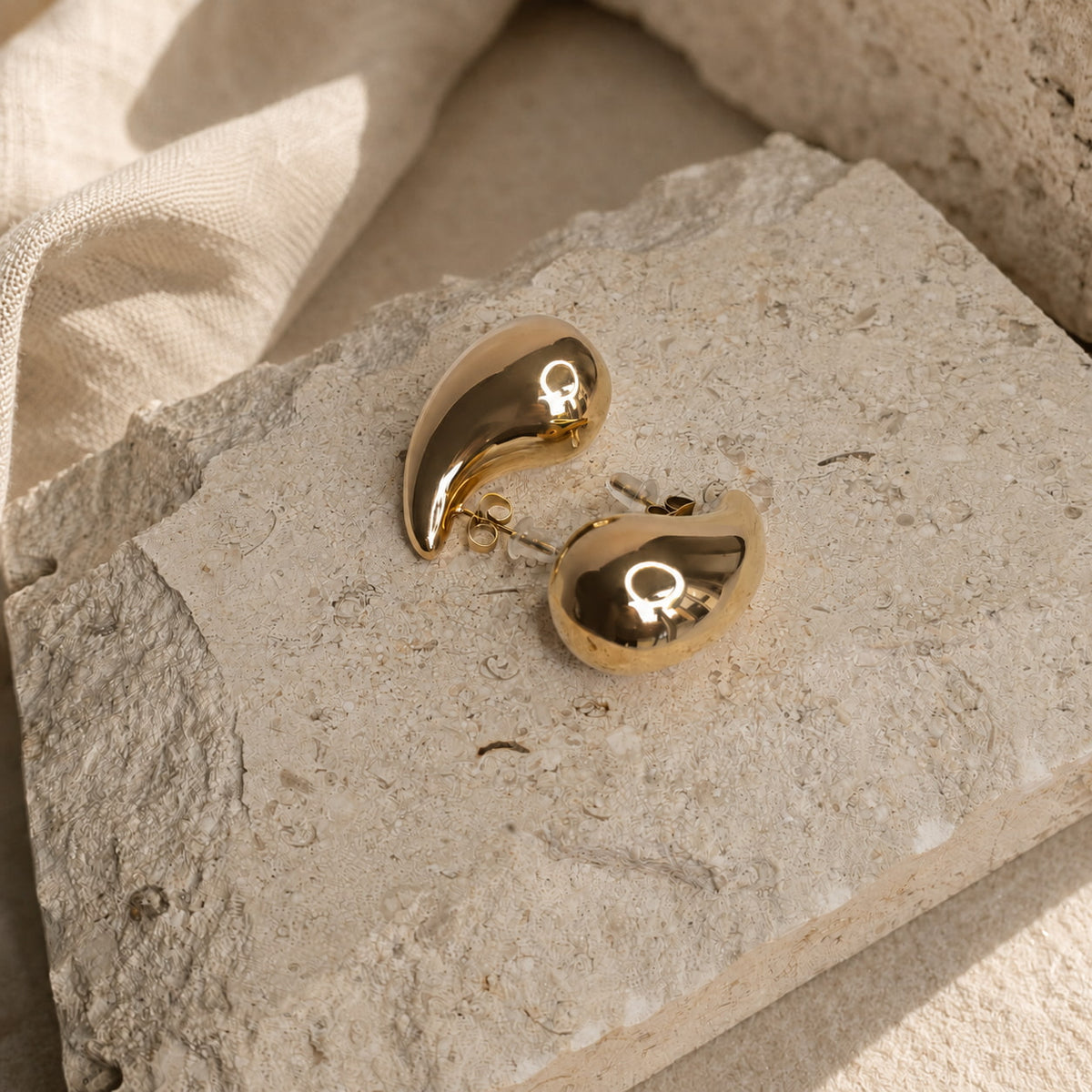Druppelvormige gouden oorbellen met glanzende finish in daglicht
