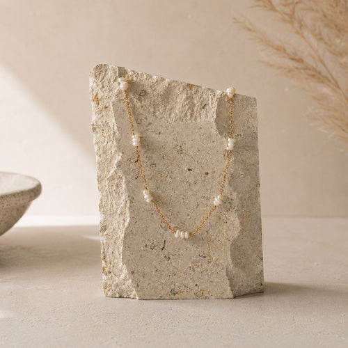 Fijne goudkleurige parelketting Bella Necklace van hi SISU op travertin steen