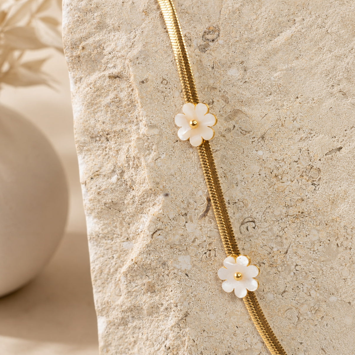 Gouden herringbone ketting met parelmoer bloemen op travertin steen