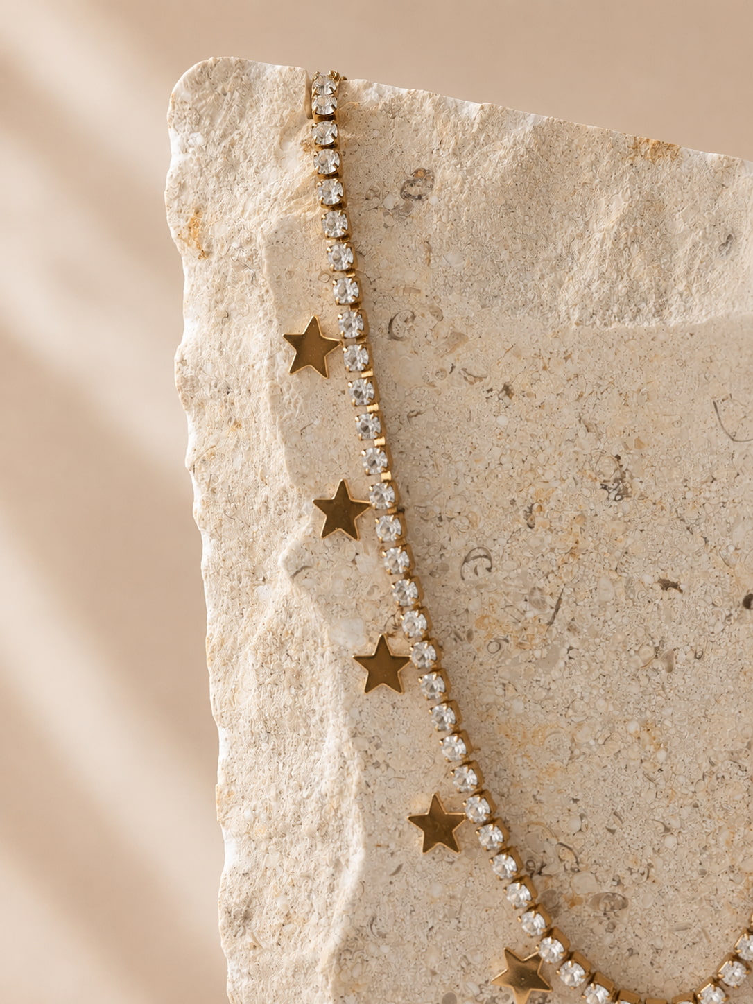 Gouden ketting met rhinestones en sterhangers op travertin steen