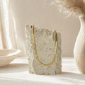 Gouden flat chain ketting op travertin steen naast keramieken vaas