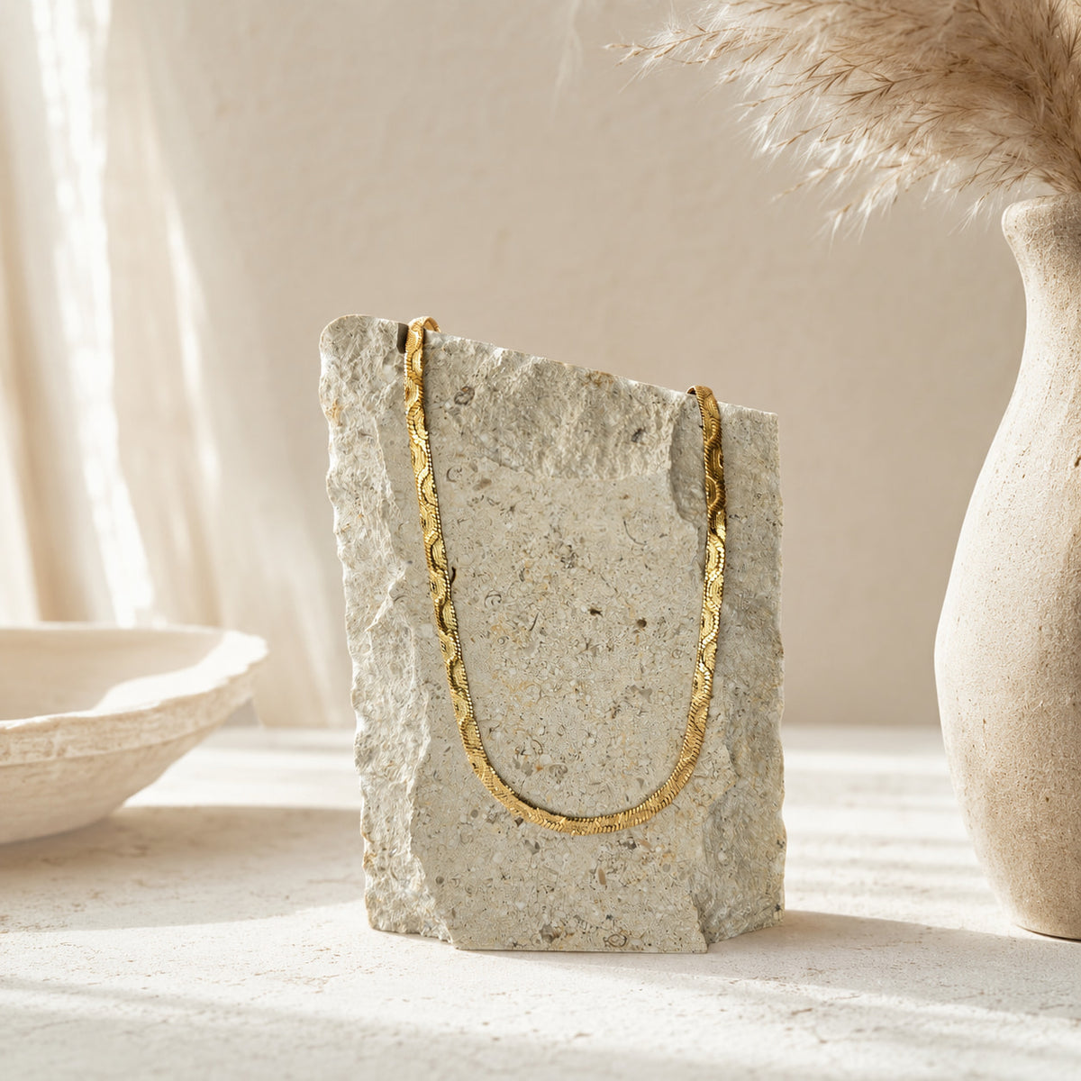 Gouden flat chain ketting op travertin steen naast keramieken vaas