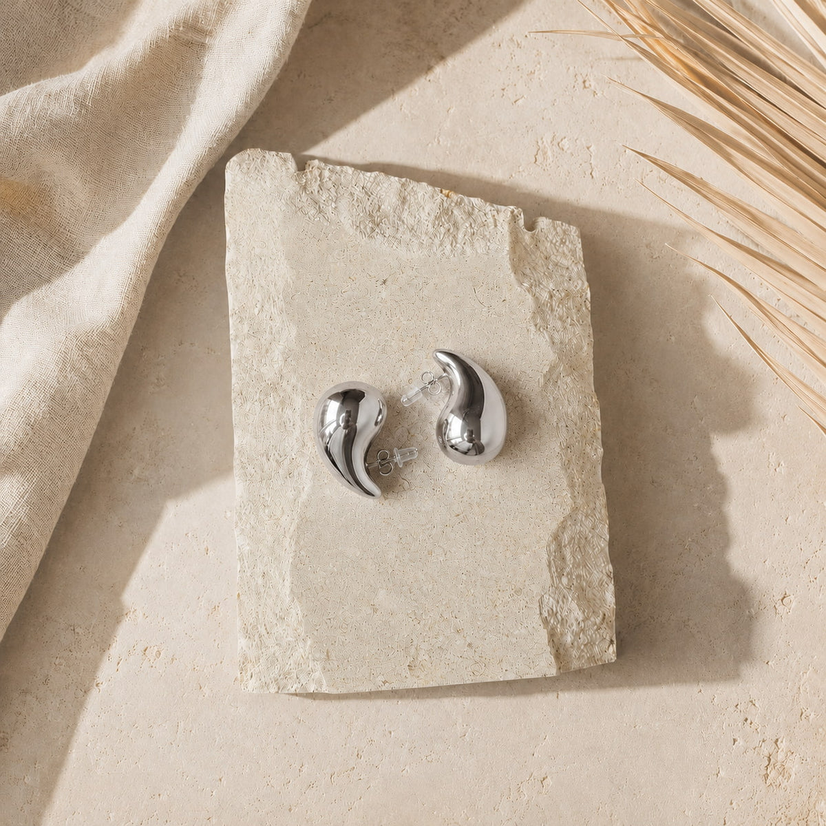 Zilverkleurige teardrop oorbellen Isabel Earrings van hi SISU, flatlay op travertin steen